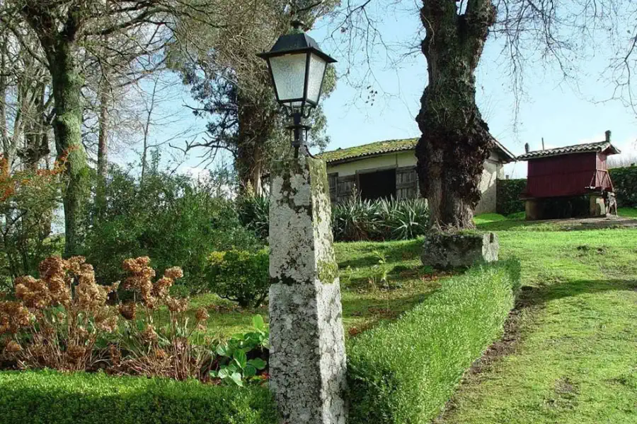 Jardín con farol de piedra, edificaciones auxiliares y hórreo gallego al fondo.
